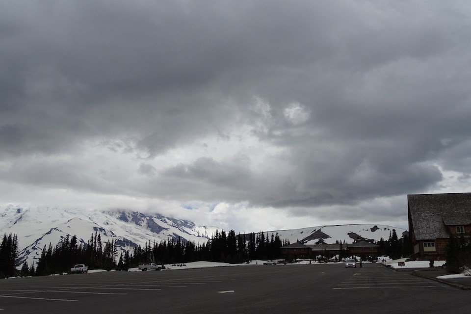 A parking lot full of cars and people with a sunny sky and Mount Rainier in the back.