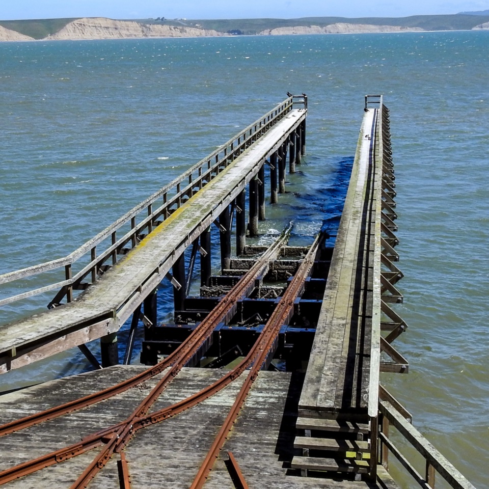 A black and white photo of uniformed men lowering an open-topped surfboat down a rail into a bay.