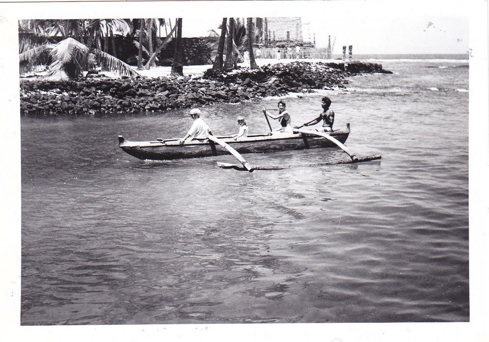 A historic photograph of a family enjoying a canoe ride in Keoneʻele Cove with Hale o Keawe in the background