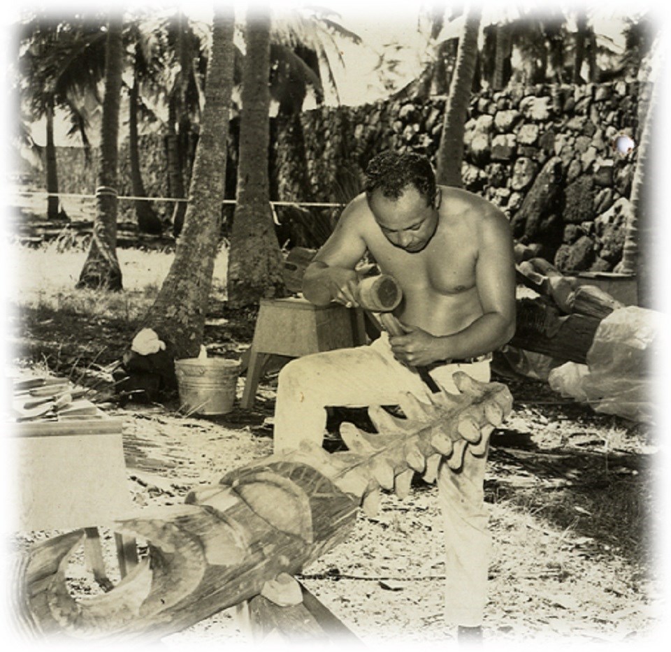 Historic photograph of a man carving a kiʻi in front of a rock wall
