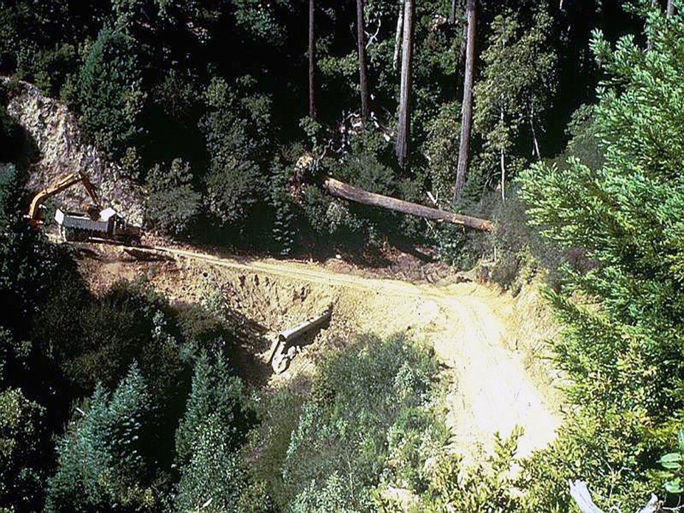 A dirt road with heavy machinery on the left, with a culvert in the middle