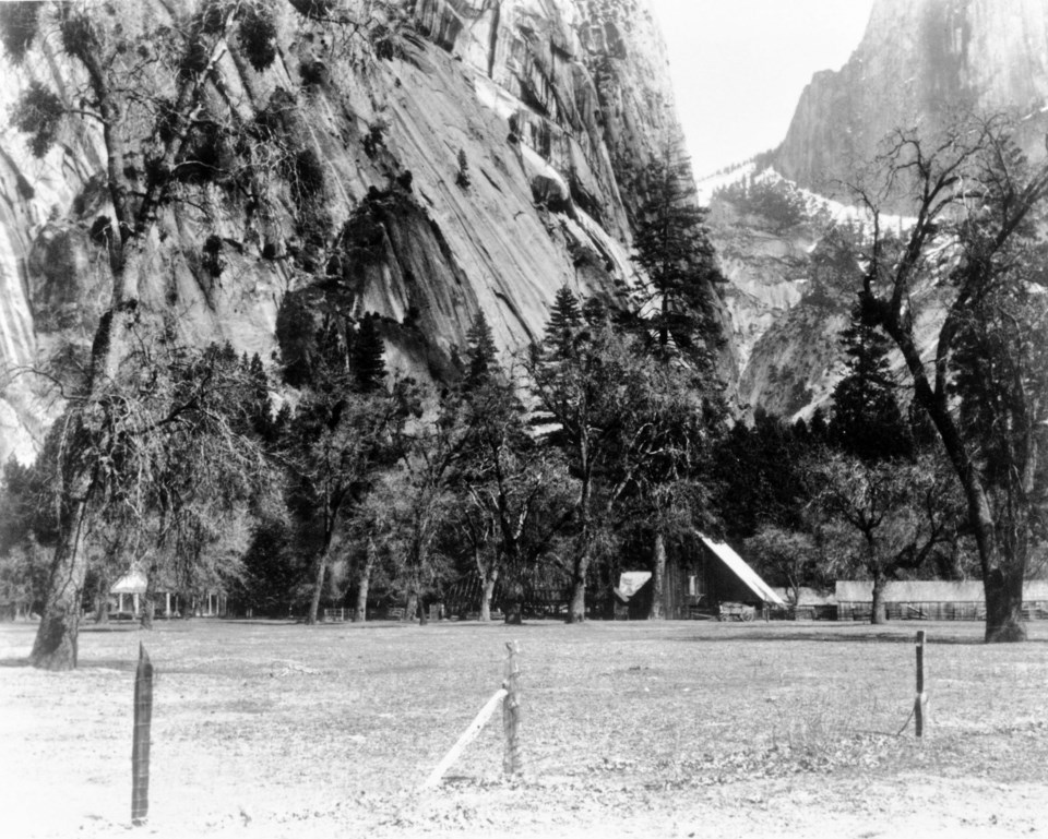 A meadow with fences and buildings, cliffs in the background.