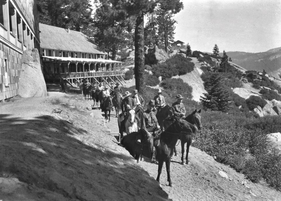 Men on horseback on a trail next to a building