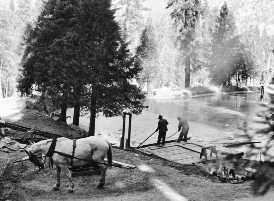 Two men and a horse next to a frozen pond surrounded by trees.