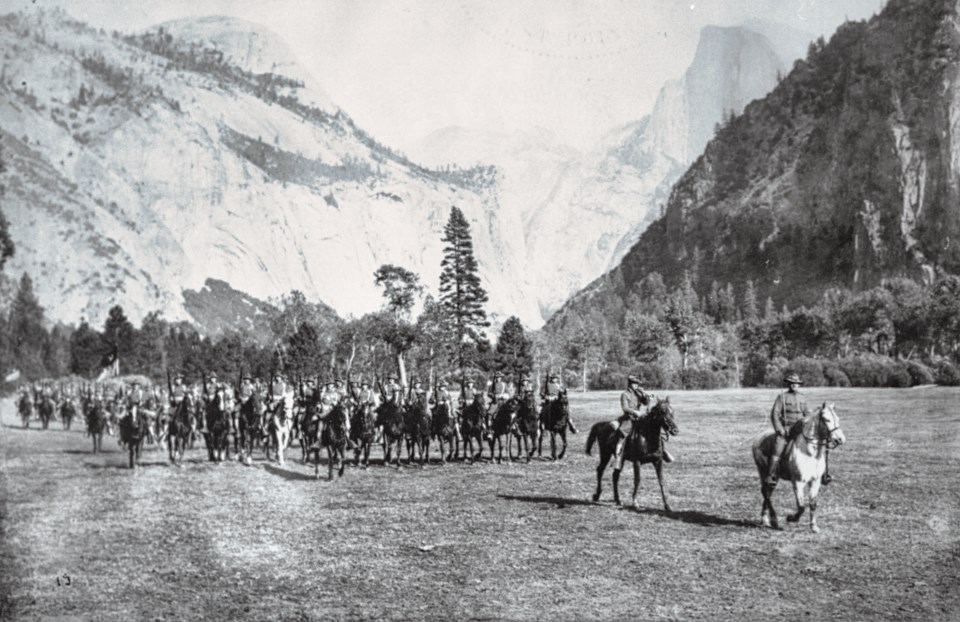 Soldiers riding horses in a meadow with granite cliffs in background.