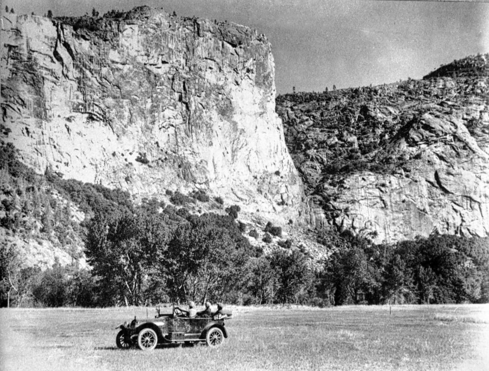 Old car in meadow in front of granite cliff.