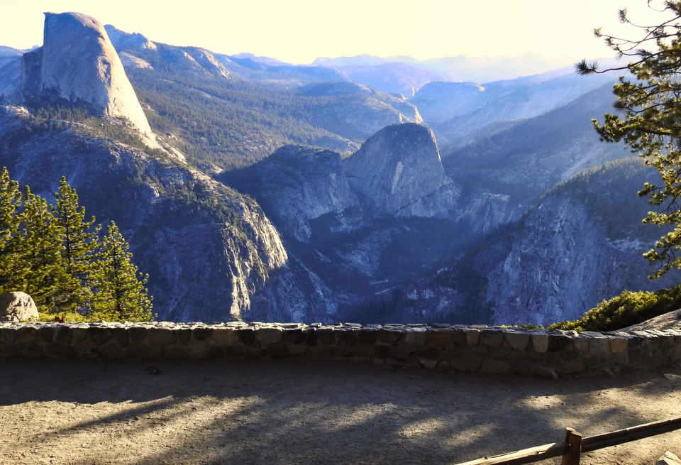 A person next to a parked older car with waterfalls and mountains in background.
