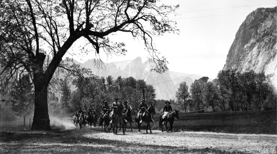 Soldiers riding horses under a tree with granite cliffs in background.