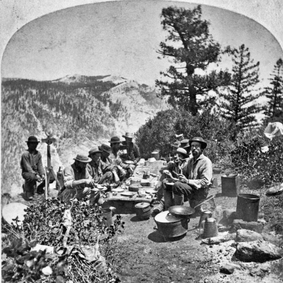 Men sit and eat at a table set up on a trail.
