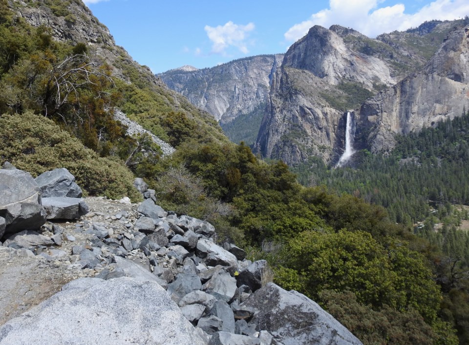 Horse-drawn stages on a road cut into the edge of a hill with cliffs in the background.