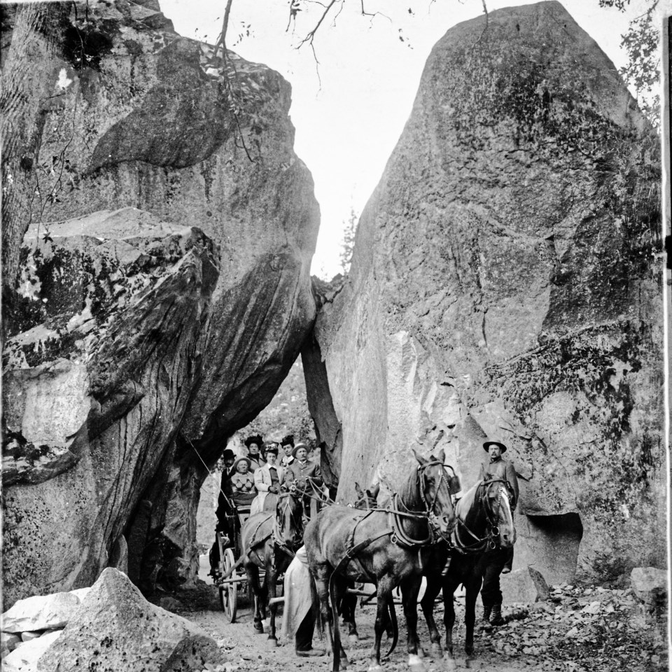 Horses and men ride through a gap between two boulders.