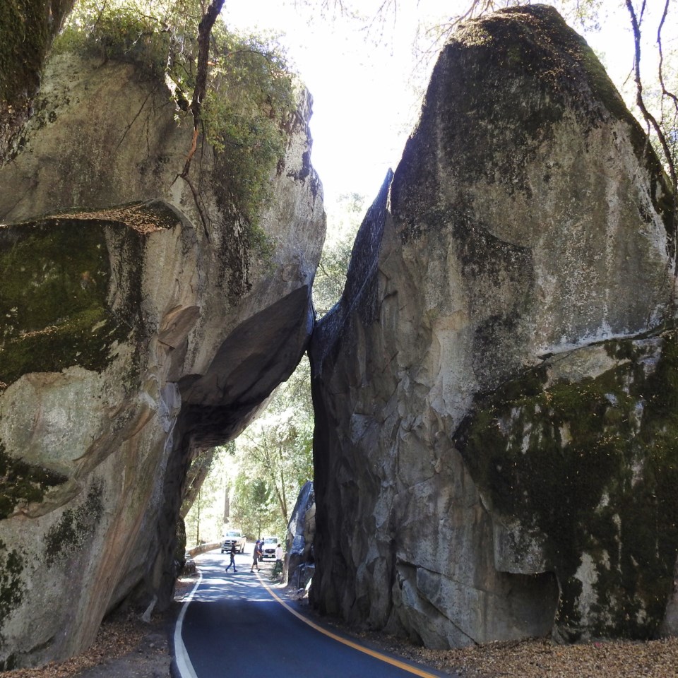 Horses and men ride through a gap between two boulders.