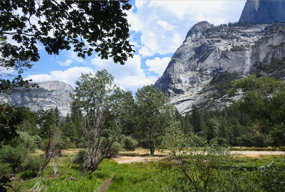 Painting of a lake, with people on the shore, and cliffs in background.