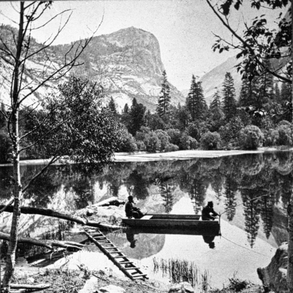 Two men in a canoe on a lake with cliffs in background.