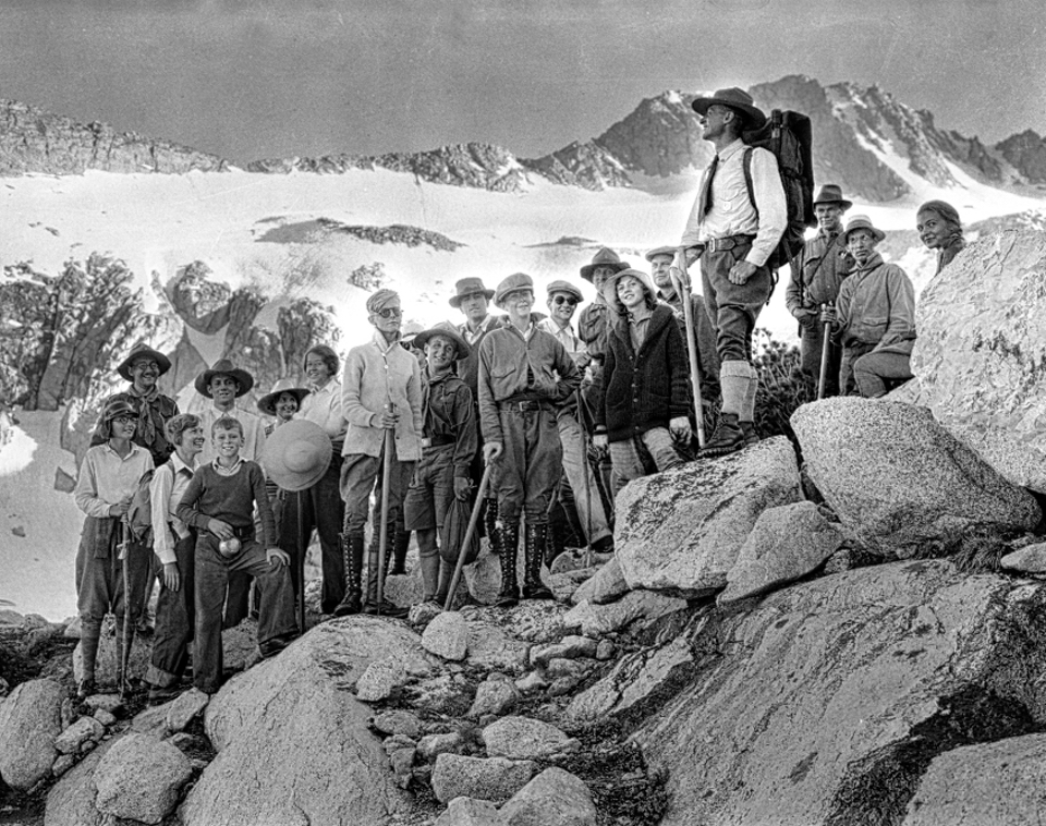 A park ranger presenting to a group of people with a glacier in background.