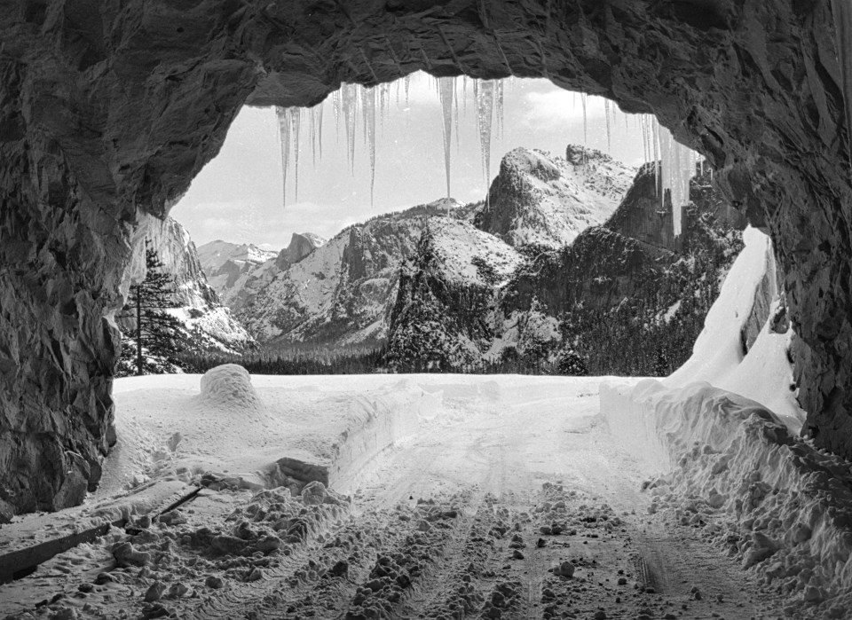 Photo from inside a tunnel with icicles, snow, and mountains visible.
