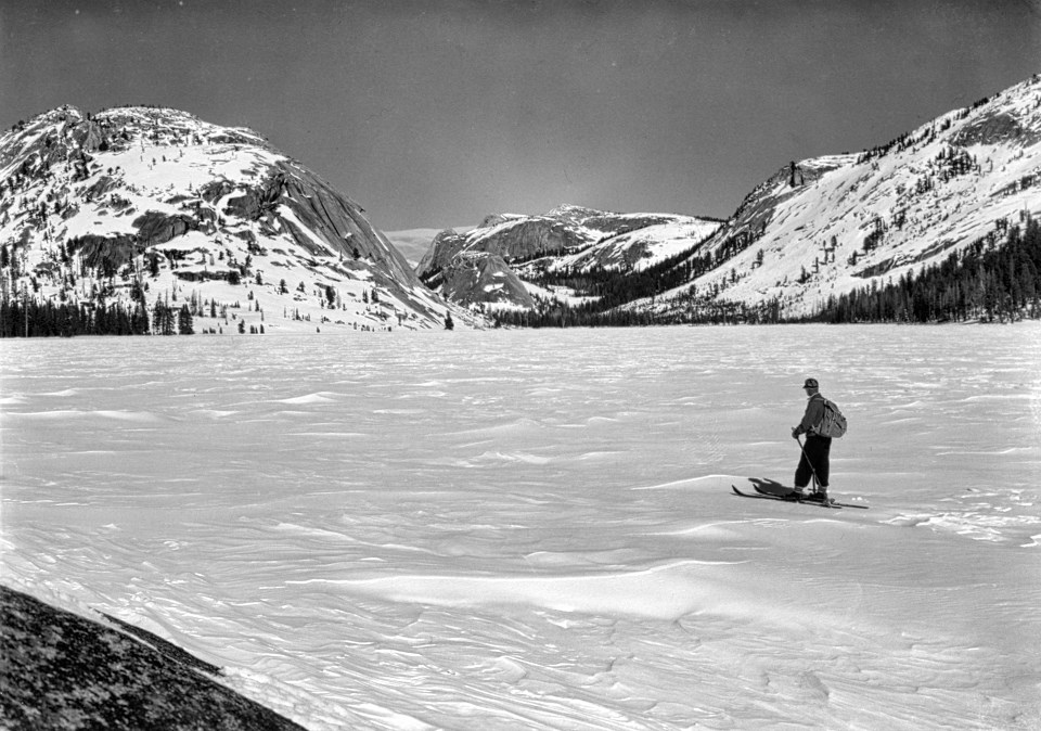 A man skiing on a lake in winter with mountains in background.