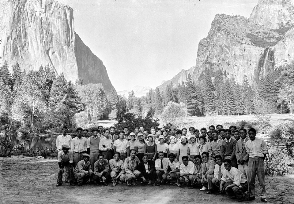 A group of people next to a river with cliffs and waterfalls behind.