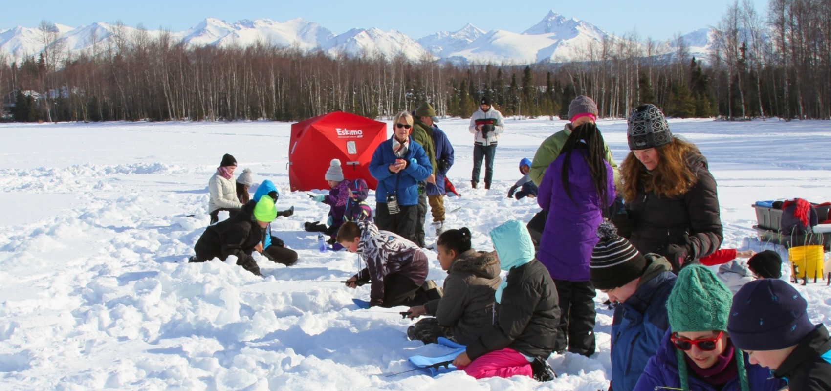 Students enjoying ice fishing on a frozen lake during a ranger-led program.