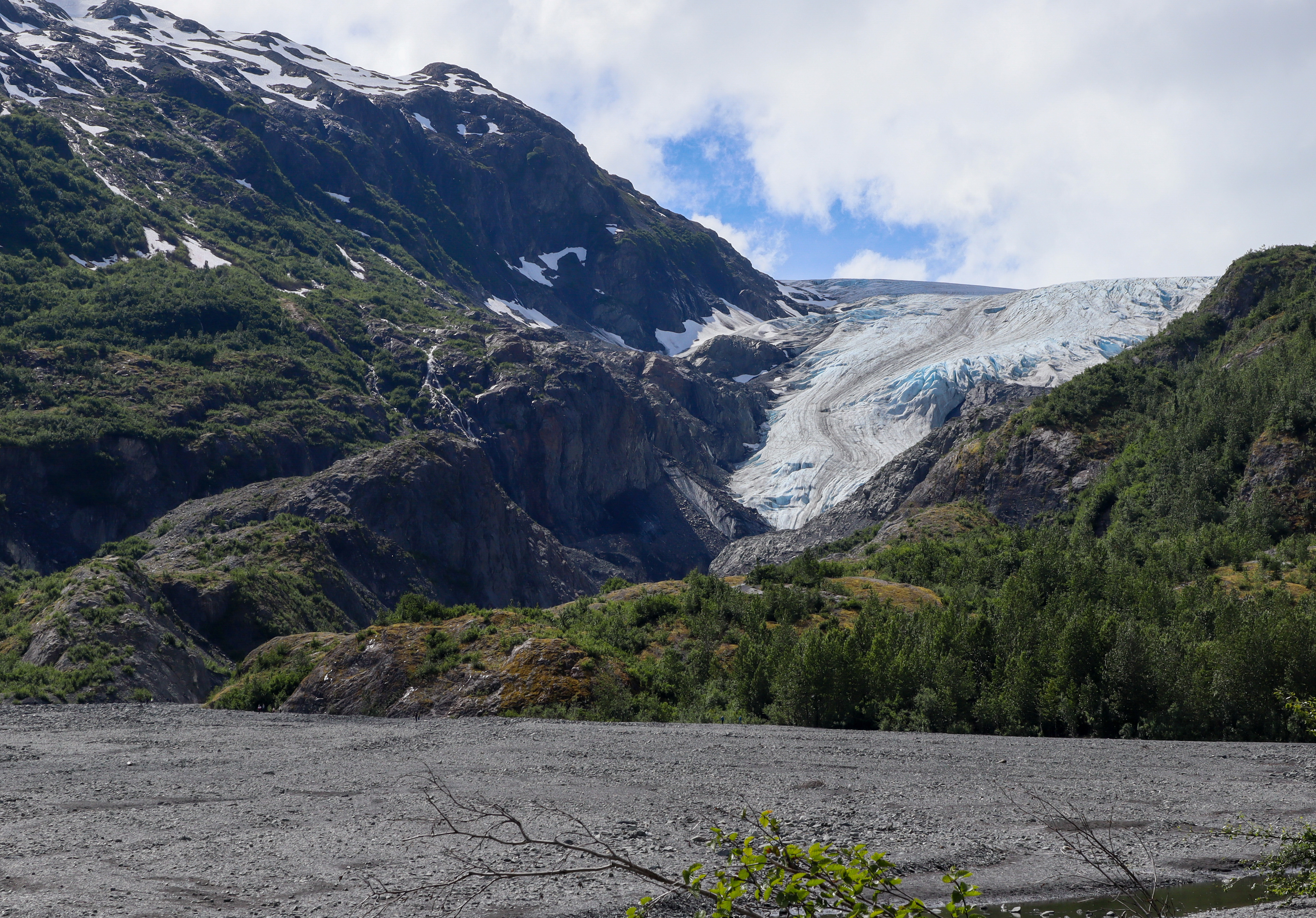 A larger glacier flows down a mountainside with with a large grey river flowing out from it.
