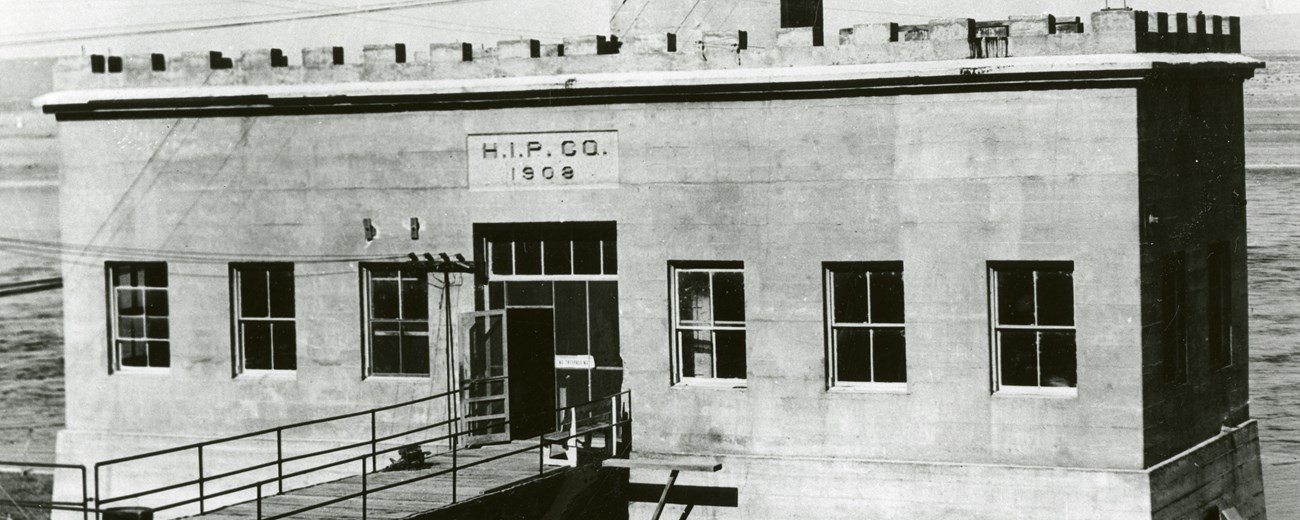 Small square cement building along a waterway. Lettering on the building reads "H.I.P.CO. 1908"
