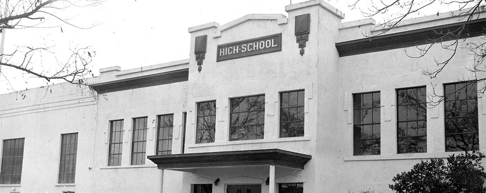 A black and white photo of a building that reads High School on a plaque.