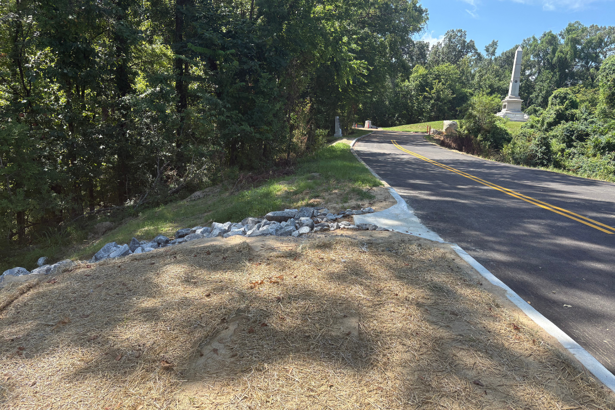 Grant Circle Road before restoration, showing severely cracked, buckled, and collapsed pavement along a wooded section of the road.