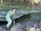 person digging next to a thick wall of ice covered by a thin layer of soil