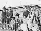 black and white image of ten adults and two kids near wooden buildings