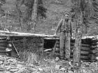 black and white image of a man near a small log cabin