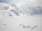 view of tents and people on a glacier, surrounded by steep mountains