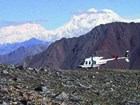 a helicopter parked on a rocky ridge, rugged mountains in the distance