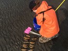 woman in an orange rain jacket kneeling on a beach near a dozen clams