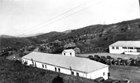 A large maintenance shed, smaller cabins, and rows of trucks are arranged across a slope.