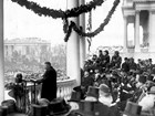 Dignitaries in formal suits listen to an inaugural speech.