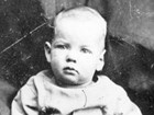 A baby in 1800s clothes sits for a portrait photo.