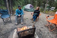 man and woman sitting by a campfire in a campground