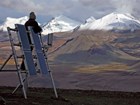 man stands on top of solar panels with snow-capped mountains in the distance