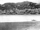 black and white photo of a man in a boat in a mountainous bay