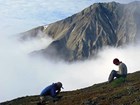 two people on a hillside overlooking a mountain shrouded in clouds