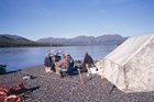 a group of people near a canvas tent, alongside a large river