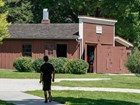 A boy walks a park path toward a historic blacksmith shop painted brown.