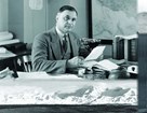 Black and white photo of Arno Cammerer sitting at his desk looking through papers.