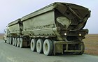 A semi-truck hauling two trailers filled with ore on a gravel road.