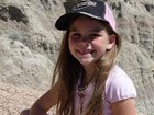 Young girl in hiking attire standing amid badlands formations on a sunny day.