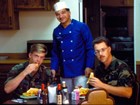 A military chef poses with two uniformed airmen at a dining room table.