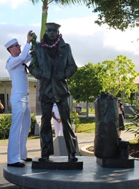 Man in navy uniform drapes a lei on the Lone Soldier monument.