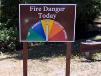 Brown sign stating Fire Danger Today, with colored wedges indicating Low to Extreme fire danger.