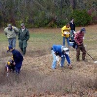Men, women and children surveying a field with metal detectors.