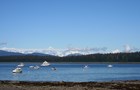 Fishing boats spread across the blue surface of water, framed by mountains and blue sky